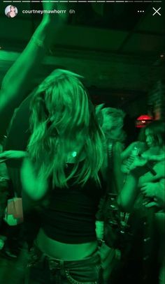 a woman is dancing in the dark with green lights on her chest and arms behind her head