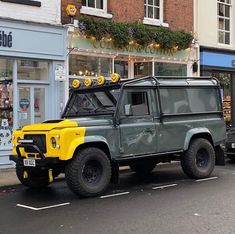 a green and yellow land rover parked on the side of the road in front of a store