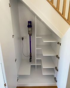 a white closet with shelves and a purple vacuum in the bottom half, under a stair case