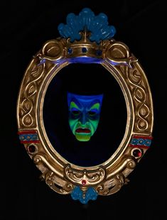 a mirror with a face painted in blue and green on the front, surrounded by gold filigrees