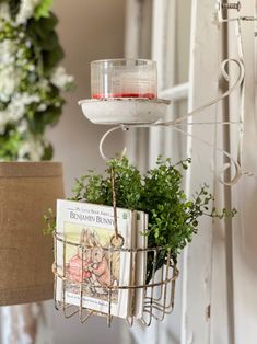 a hanging basket filled with books next to a lamp and potted plant on top of a table