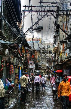 many people are walking through an alleyway in the rain with power lines above them