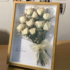 a bouquet of white flowers in a wooden frame on a table with pictures behind it