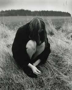 a woman kneeling down in the middle of a field with her hands on her knees