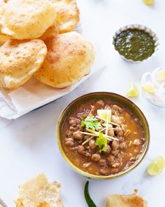 a bowl filled with beans and bread next to some dipping sauce on a white table