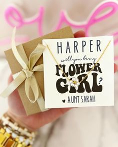 a person holding a flower girl card in their hand with a bow on it's neck