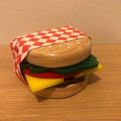 a toy hamburger with cheese, pickles and ketchup sitting on a wooden table