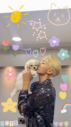 a woman kissing a small white dog in front of a wall with hearts and stars on it