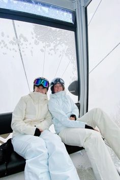 two people sitting on a ski lift wearing snow suits and goggles, with their arms around each other