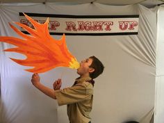 a young boy holding up a fake fireball in front of a white backdrop with red writing on it