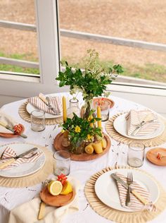 the table is set with plates, silverware and lemons in front of a window