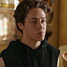 a young man with curly hair wearing a black hoodie and looking at the camera