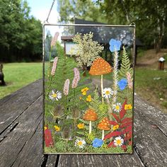 a glass block with flowers and mushrooms on it sitting on a wooden table in the grass