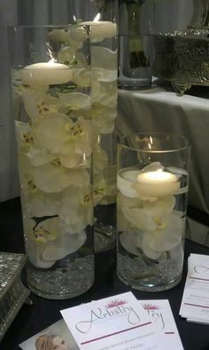 two vases filled with water and flowers on top of a table next to cards