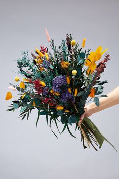 a bouquet of flowers being held by someone's hand in front of a gray background