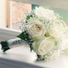 a bouquet of white roses and baby's breath sits on a window sill