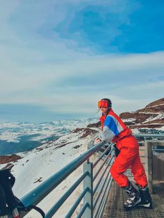 a man standing on top of a snow covered slope next to a metal fence and railing