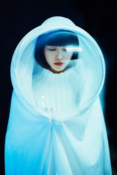 a woman in a white sweater is looking through a plastic covering over her head and holding a cell phone to her ear