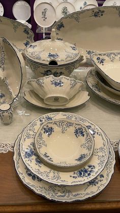 an assortment of blue and white china sitting on top of a wooden table next to plates