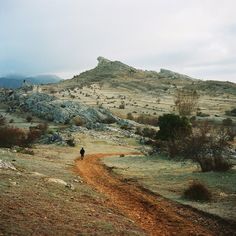 a person walking down a dirt road in the middle of a dry grass covered field