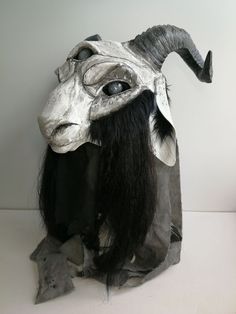 an animal mask with long black hair and horns on it's head, sitting in front of a white wall