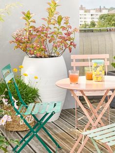 two chairs and a table on a wooden deck with potted plants in the background