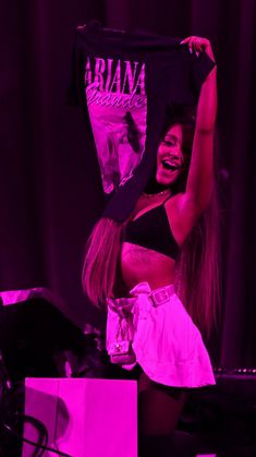 a woman holding up a t - shirt in front of her face while standing on stage