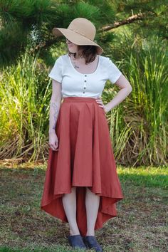 a woman standing in the grass wearing a red skirt and white shirt with her hands on her hips