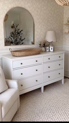 a white dresser sitting in a living room next to a chair and table with a mirror on it