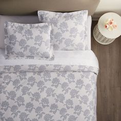 a bed with white and blue floral comforter on it's headboard next to a night stand