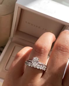 a woman's hand holding an engagement ring in her left hand, with the box open