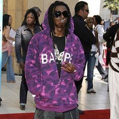 a man in a purple camo hoodie and sunglasses standing on a red carpet