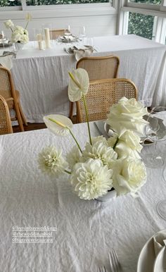 white flowers are in a vase on a table set with silverware and napkins