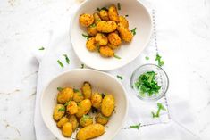 two white bowls filled with cooked potatoes on top of a table next to a glass of water