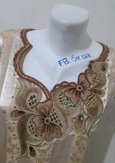 a white mannequin with gold and brown designs on it's neckline