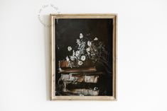 a painting hanging on the wall next to a vase with flowers in it and an old book