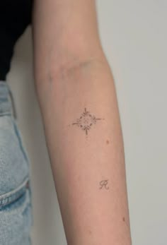 a woman's arm with a small compass tattoo on the left side of her arm