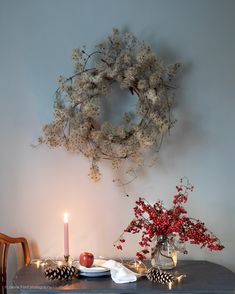 a table topped with a vase filled with flowers next to a lit candle and wreath