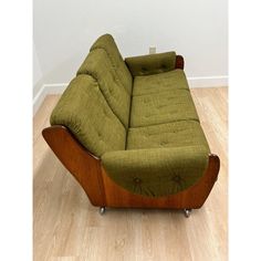 a green couch sitting on top of a hard wood floor next to a white wall