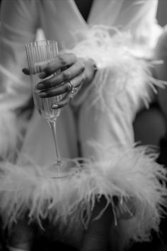 black and white photograph of a woman holding a wine glass with feathers on her arm