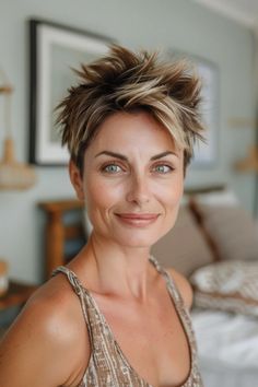 Smiling person with short, spiky hair stands in a warmly lit room.