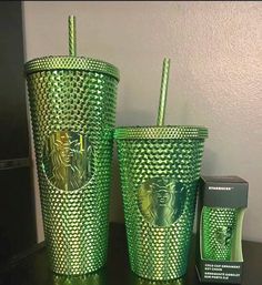 two green cups sitting on top of a table next to a cup with a straw in it