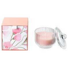 a candle in a glass container next to a pink box with flowers on the inside