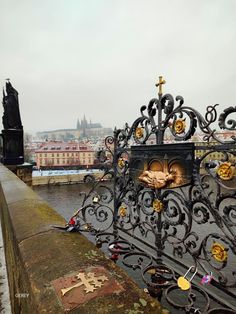 an iron fence that has been decorated with gold and crosses on it, along the river