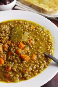 a white plate topped with lentils and carrots next to bread on a table