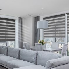 a living room filled with white furniture and windows covered in grey shades on top of them