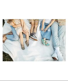 four people sitting on top of a blanket in the grass with their feet propped up against each other