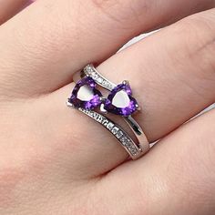 a woman's hand with a purple and white heart shaped ring on her finger