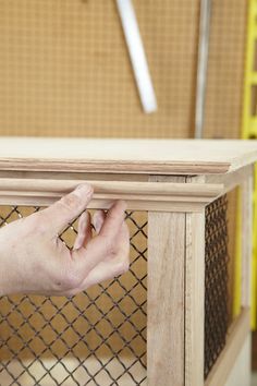 a hand is holding the edge of a piece of wood that is attached to a wire mesh fence