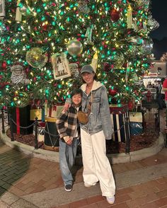 two people standing in front of a christmas tree with lights and decorations on the top